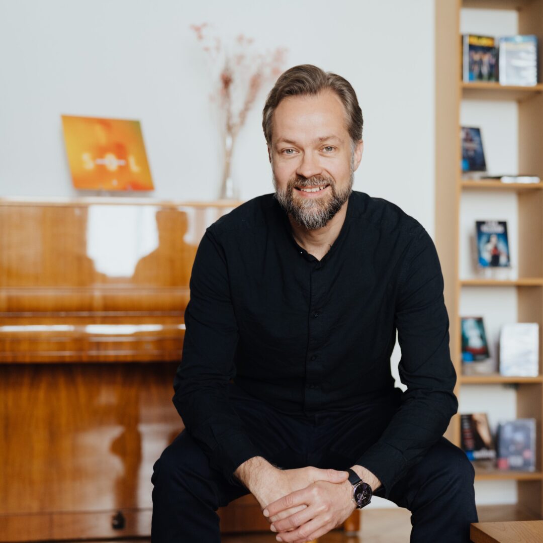 Marcus_28. April 2026 Patrick_Lipke 24_quadrat Porträt von Marcus Heinicke, Director Classics, sitzend vor einem Klavier in einem Büro- oder Besprechungsraum.
