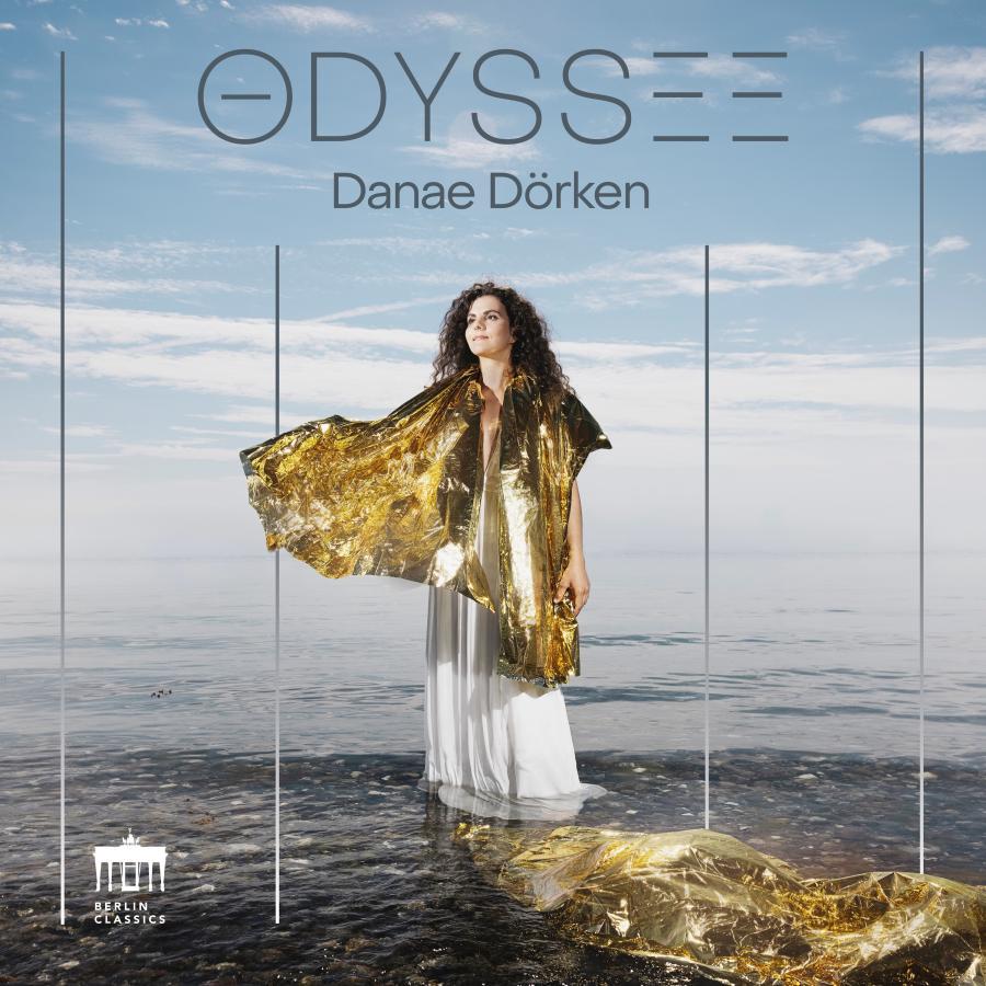 Release-Cover „Odyssee“ von Pianistin Danae Dörken. Danae Dörken in weißem Kleid mit goldener Folie am Meer, vor weitem Himmel und Wasserfläche; helle Blau-, Grau- und Goldtöne, frontale Außenaufnahme und poetische, weite Stimmung.