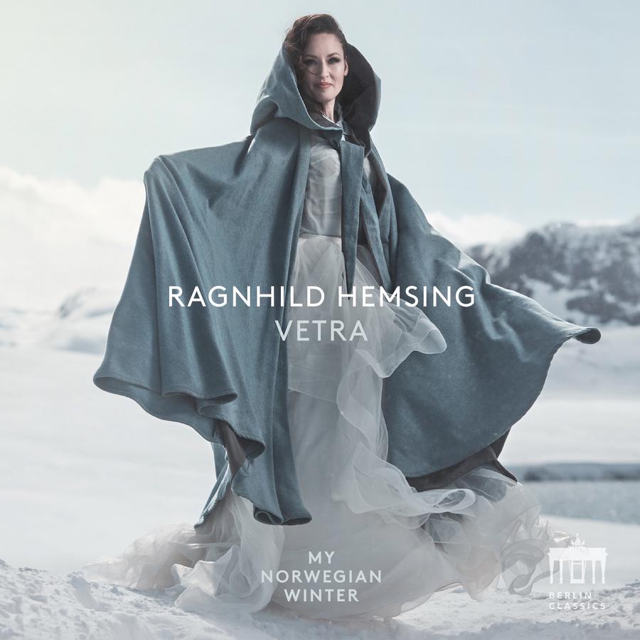 Release-Cover „Vetra“ von Violinistin Ragnhild Hemsing. Ganzkörperporträt in weitem graublauem Mantelkleid in verschneiter Winterlandschaft; kühle Weiß- und Blautöne, frontale Pose und helle, nordische Lichtstimmung.
