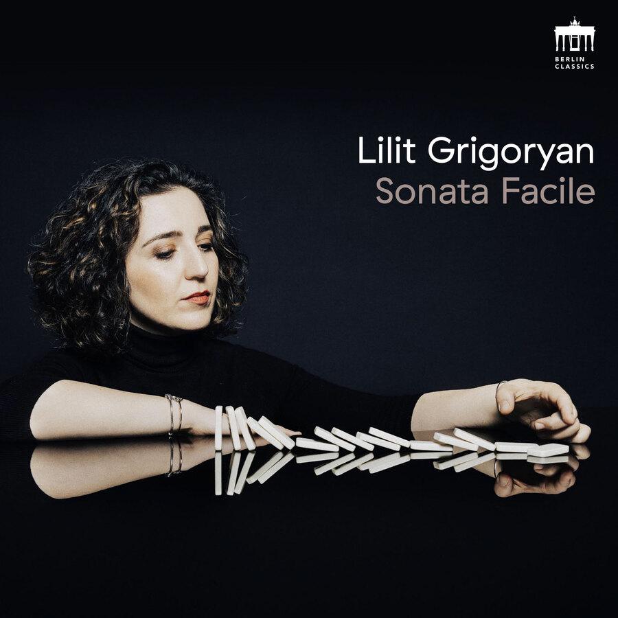 Release-Cover „Sonata Facile“ von Pianistin Lilit Grigoryan. Dunkles Porträt mit spiegelnder schwarzer Fläche und umgefallenen Domino-Steinen; seitliche Nahaufnahme, starke Kontraste und ruhige, konzentrierte Lichtstimmung.