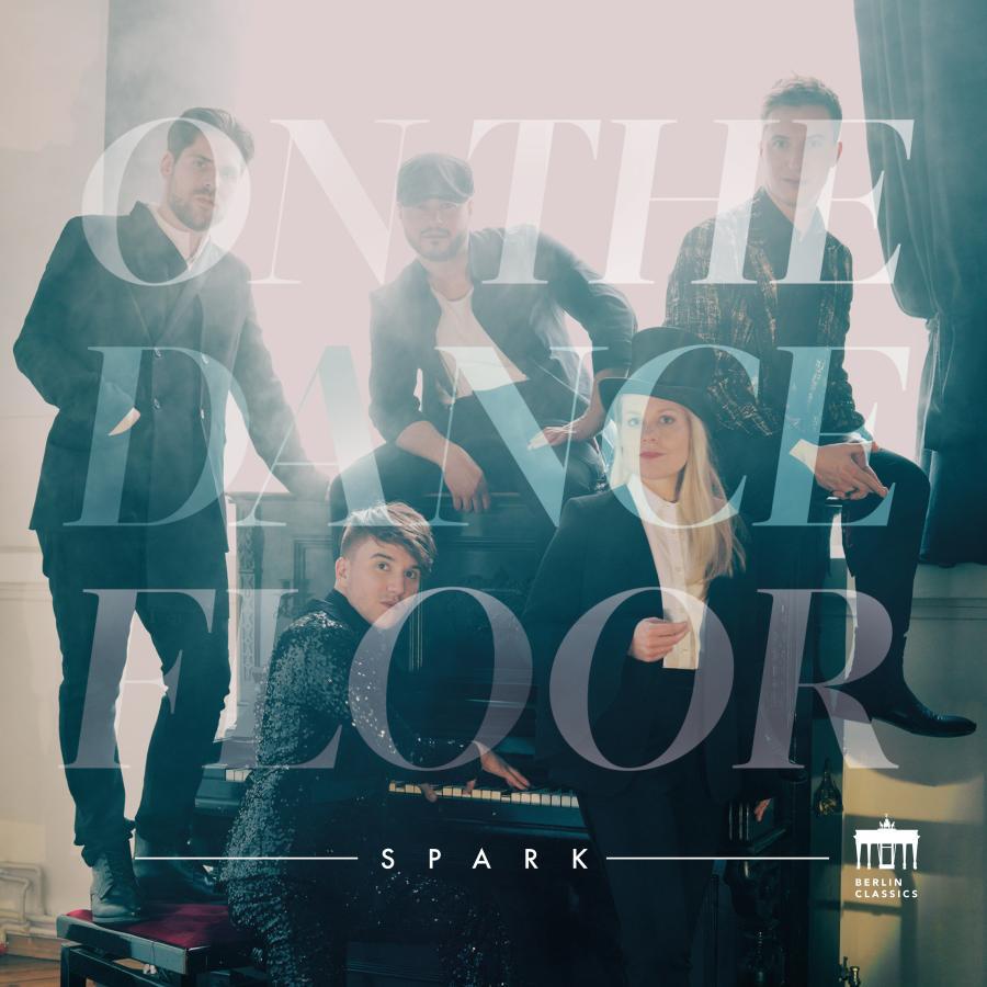 Release-Cover „On the Dancefloor“ vom Ensemble Spark. Helles Gruppenfoto von fünf Musiker:innen in einem Innenraum mit großer transparenter Typografie über dem Bild; kühle Türkis- und Weißtöne, weiches Gegenlicht und stilisierte Club-Atmosphäre.