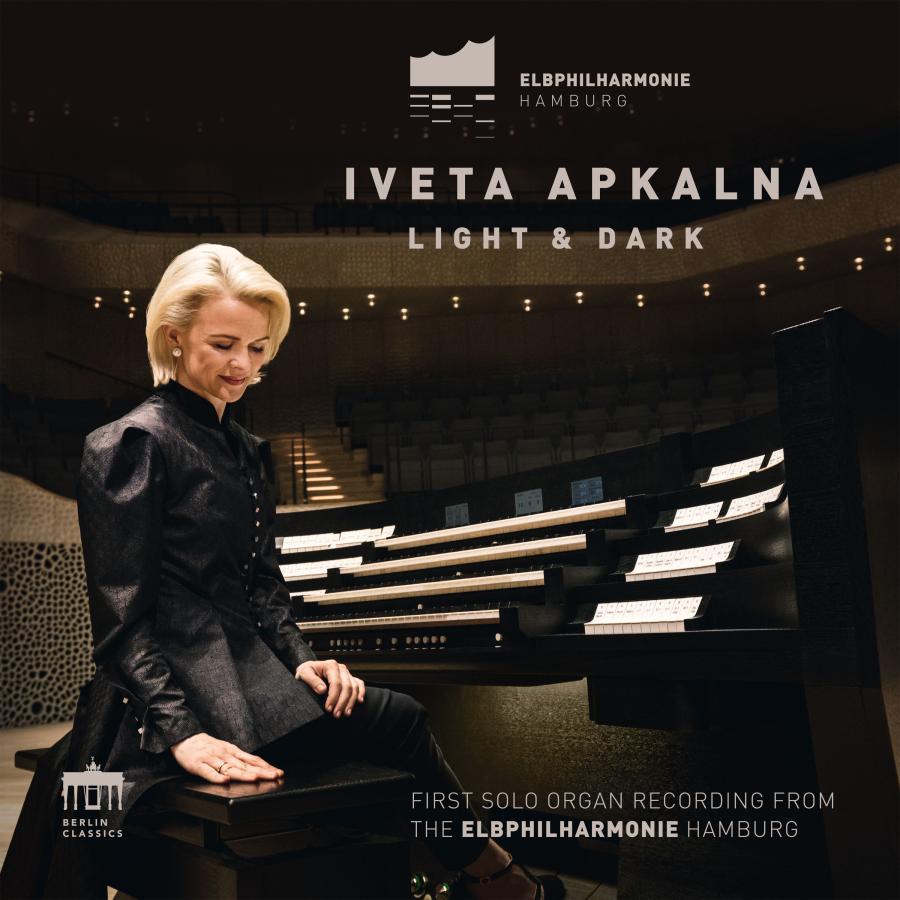 Release-Cover „Light & Dark“ von Organistin Iveta Apkalna, aufgenommen in der Elbphilharmonie Hamburg. Iveta Apkalna sitzt einer großen Orgel in dunklem Konzertsaal und schaut schräg nach unten; warme Lichtpunkte, starke Schatten und elegante, konzentrierte Atmosphäre.