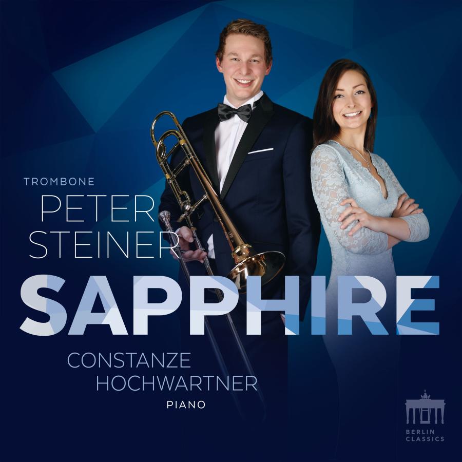 Release-Cover „Sapphire“ von Posaunist Peter Steiner und Pianistin Constanze Hochwartner. Beide Musiker:innen vor dunkelblauem, geometrischem Hintergrund, Peter Steiner hält eine Posaune; kühle Blautöne, frontale Studioaufnahme und moderne Konzertwirkung.