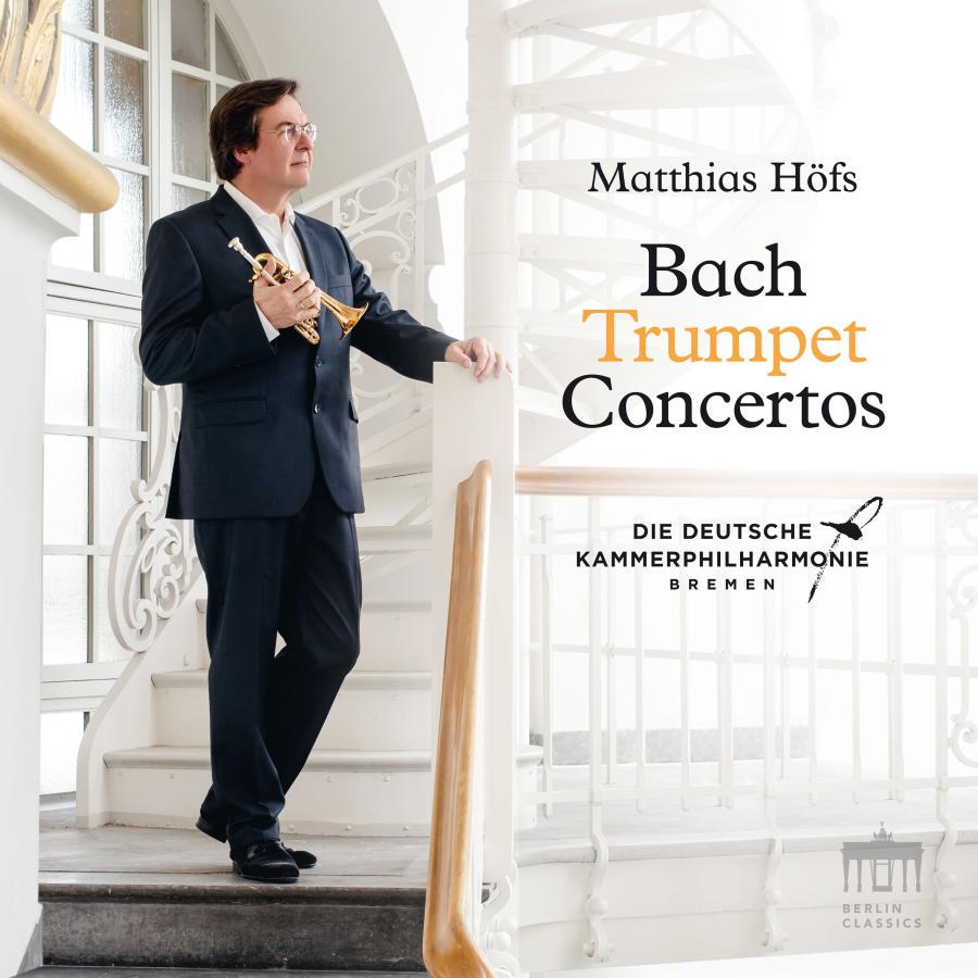 Release-Cover „Bach: Trumpet Concertos“ von Trompeter Matthias Höfs mit der Deutschen Kammerphilharmonie Bremen. Helles Porträt von Höfs im Anzug mit Trompete auf einer weißen Treppe; luftige Innenraumperspektive, weiches Licht und elegante Konzertatmosphäre.