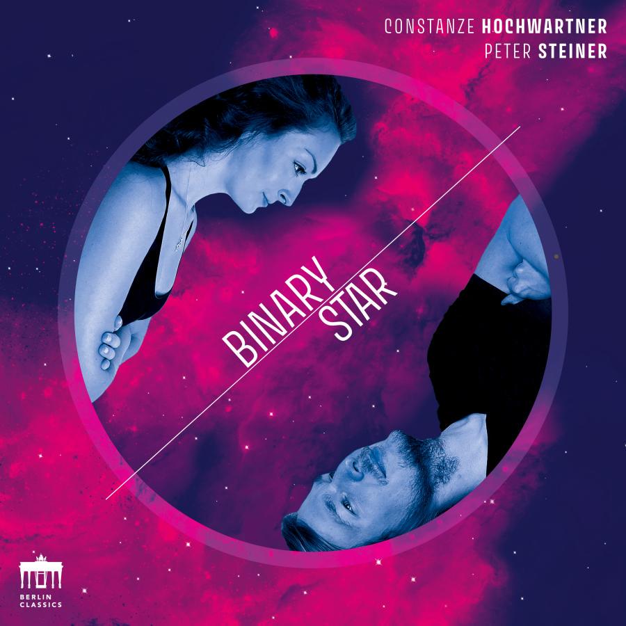 Release-Cover „Binary Star“ von Organistin und Pianistin Constanze Hochwartner und Peter Steiner. Kosmische Grafik mit zwei gegenüberliegenden Porträts in einem Kreis vor pink-violettem Sternennebel; kühle Blautöne, leuchtende Magenta-Akzente und futuristische Frontalansicht.