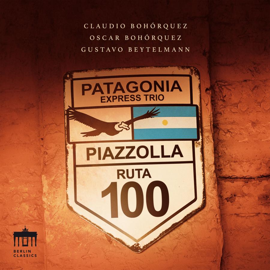 Release-Cover „Piazzolla: Patagonia Express Trio“ mit Cellist Claudio Bohórquez, Oscar Bohórquez und Gustavo Beytelmann. Metallschild auf dem „Patagonia Express Trio“ und „Ruta 100“ steht, ist an einer warm beleuchteten Backsteinwand angebracht; Orange- und Brauntöne, frontale Perspektive und lateinamerikanische Reiseästhetik.