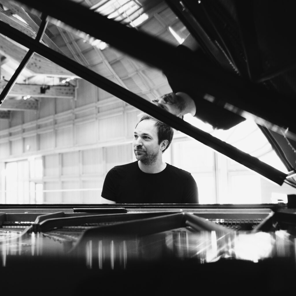 Pianist Herbert Schuch sitzt am geöffneten Flügel, schwarz-weiß Aufnahme