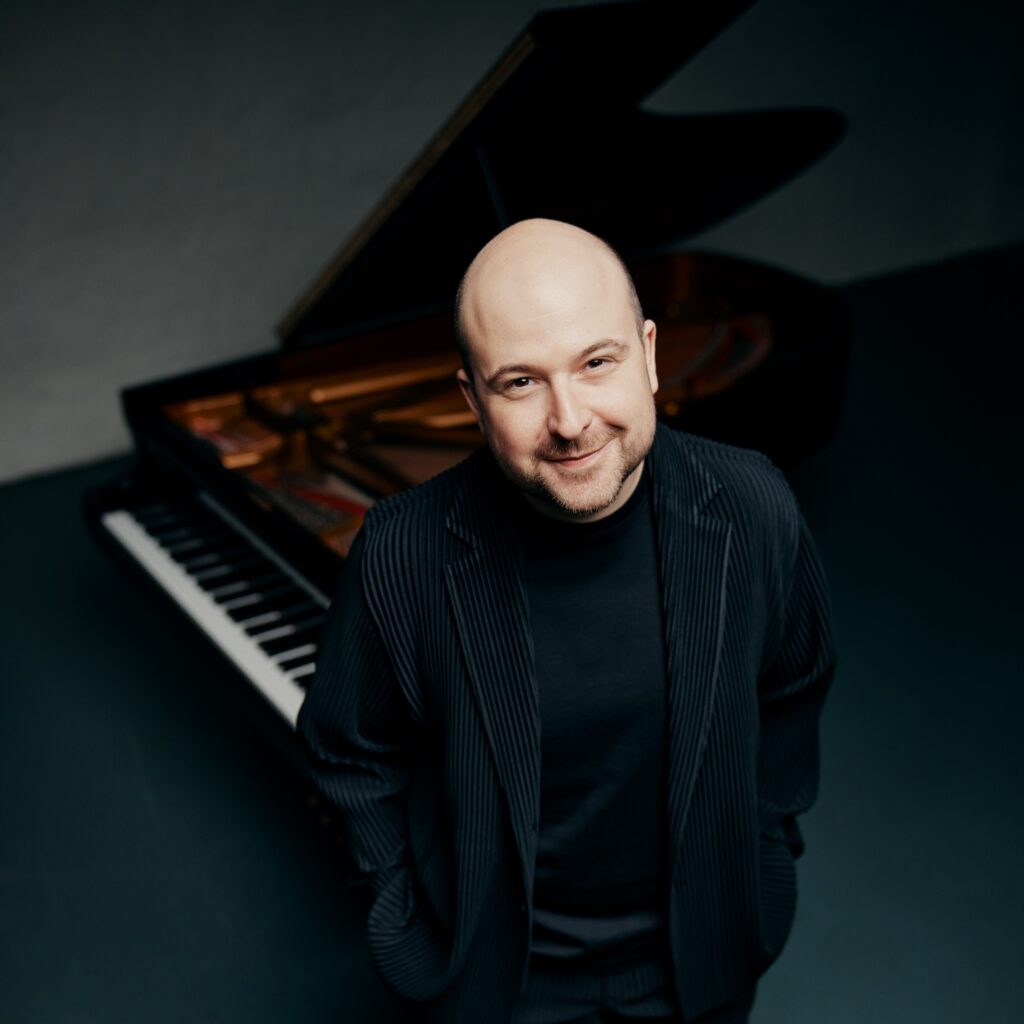 Moritz Winkelmann steht im Raum und schaut in die Kamera, im Hintergrund ist ein Grand Piano