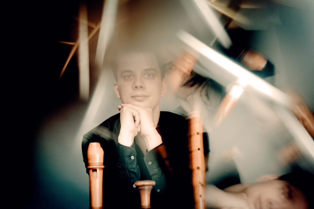 Portrait Blöckflötist Max Volbers, bei dem er den Kopf auf seinen Händen abstützt mit Flöten senkrecht im Vordergrund und durch Prisma gebrochene Lichteffekte.